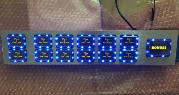 A rectangular object with blue lights is the WMS BBII OLED 3.0 S/T Complete Button Deck. GETT Part BP105.