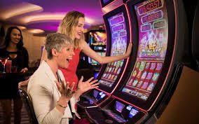 Two women playing slot machines in a casino.