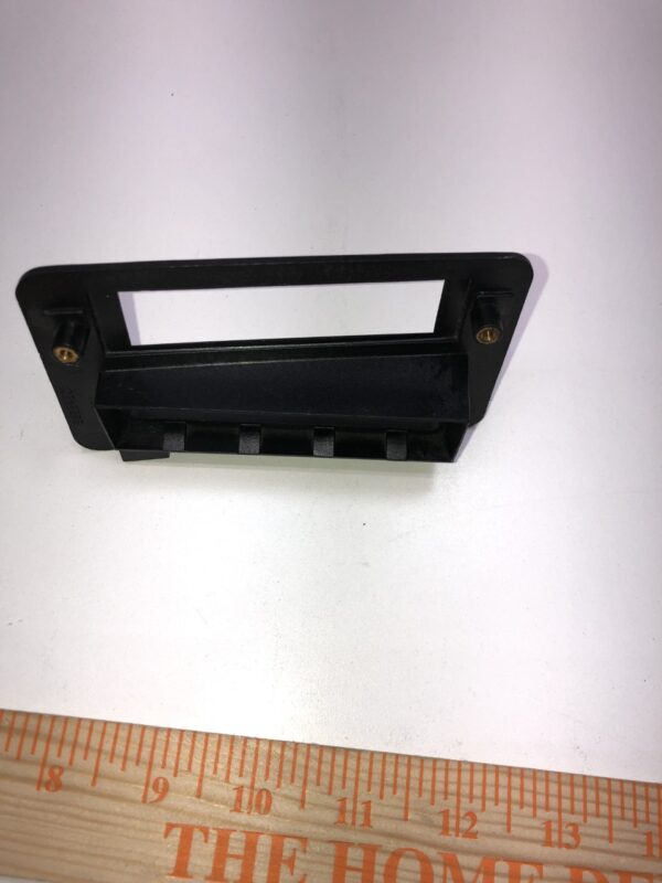 A Ticket Printer Bezel, Stock, Non Lit, Black Plastic on top of a ruler.