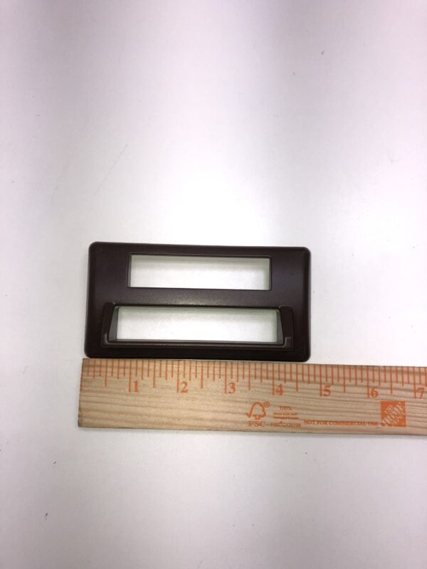 A Ticket Printer Bezel, Black/ Plastic with a ruler next to it.