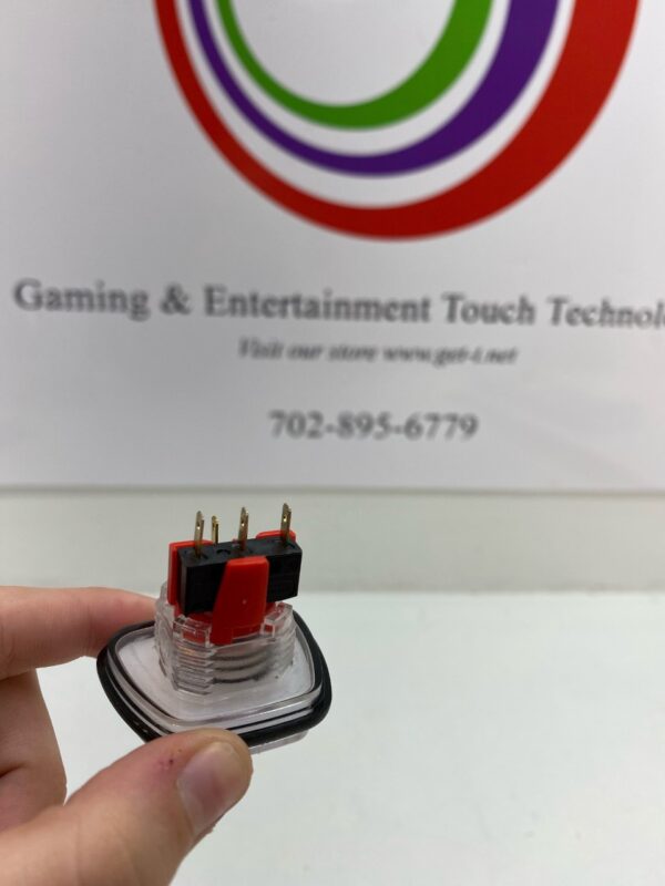A person holding a red and black Plastic Push button, 4 sided trapezoid with the GamesMan logo on it.