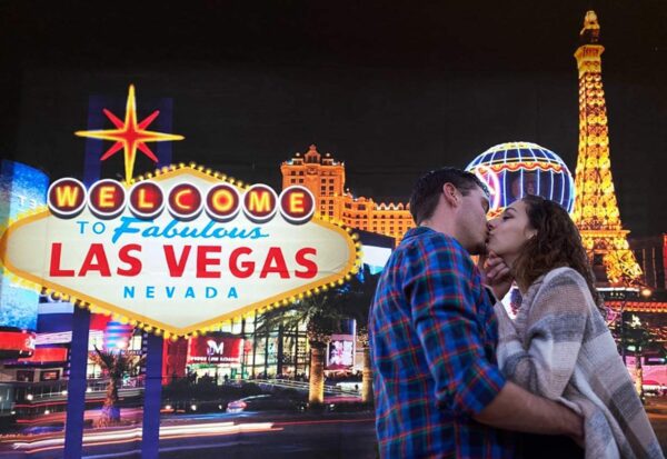 A couple kisses in front of the Welcome to Las Vegas Backdrop Casino City Night Scenery Background 7x5ft Vinyl Billboard Banner Themed Party Decoration Backdrops. GETT Part CQD103.