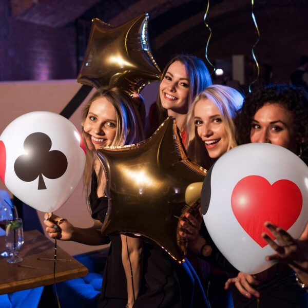 A group of women holding up 12 Inch Casino Card Night Latex Balloons at a party.