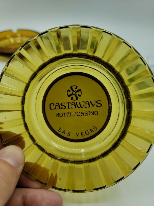 A person is holding a yellow plate with the word Vintage Las Vegas Casino Ashtrays Bally's Castaways Peppermill Hilton on it.