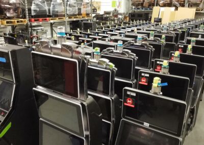 Rows of slot machines stored in a warehouse, featuring multiple screens and various colorful game decals.